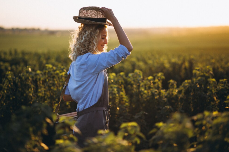 Woman adjusting hat in a vineyard at sunset